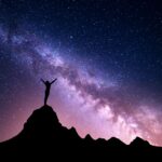 a woman standing on a mountain top with the milky way behind her