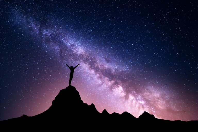 a woman standing on a mountain top with the milky way behind her