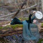 a woman lying on a log beating a drum